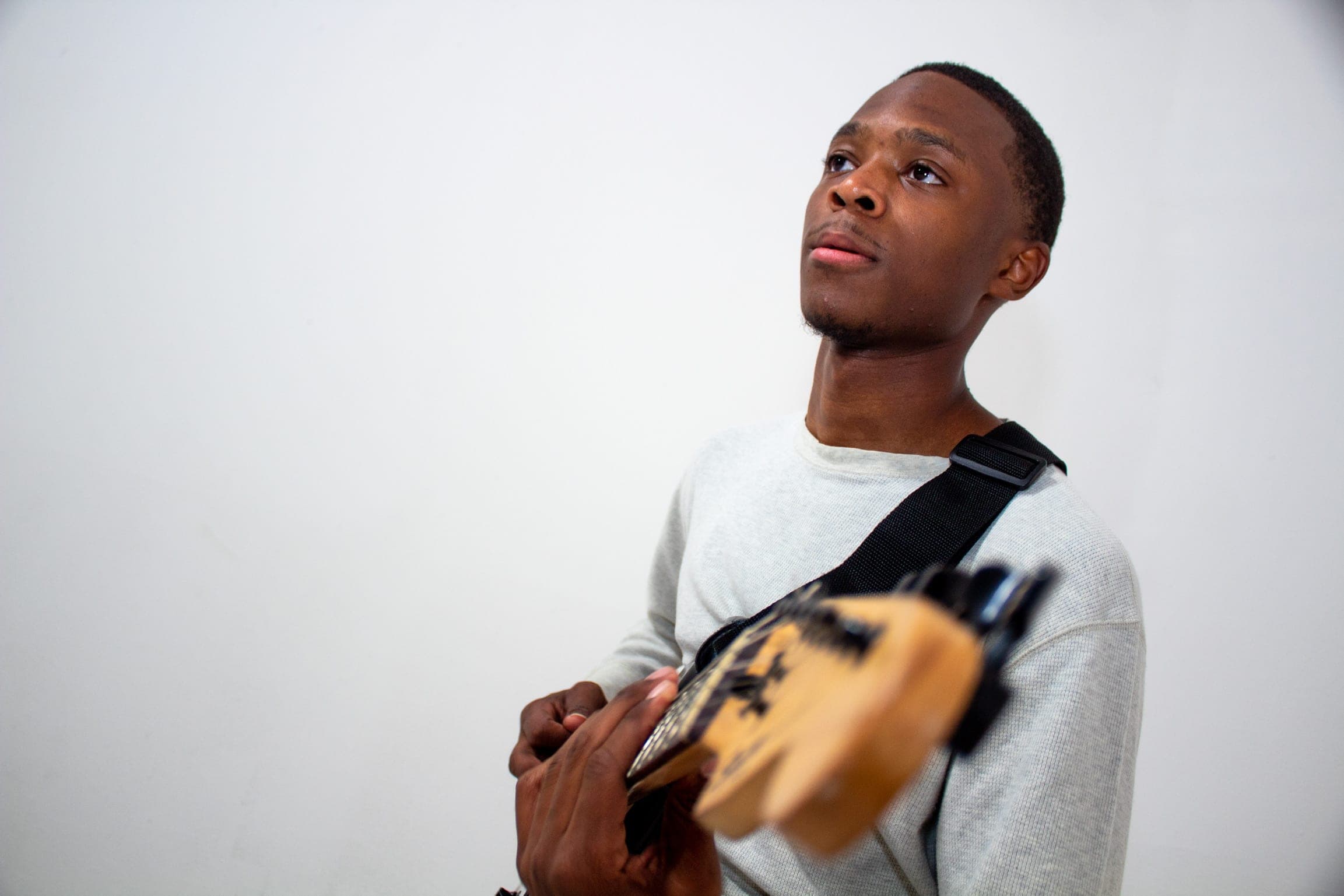Paul Neil looking up, holding his guitar in a white studio