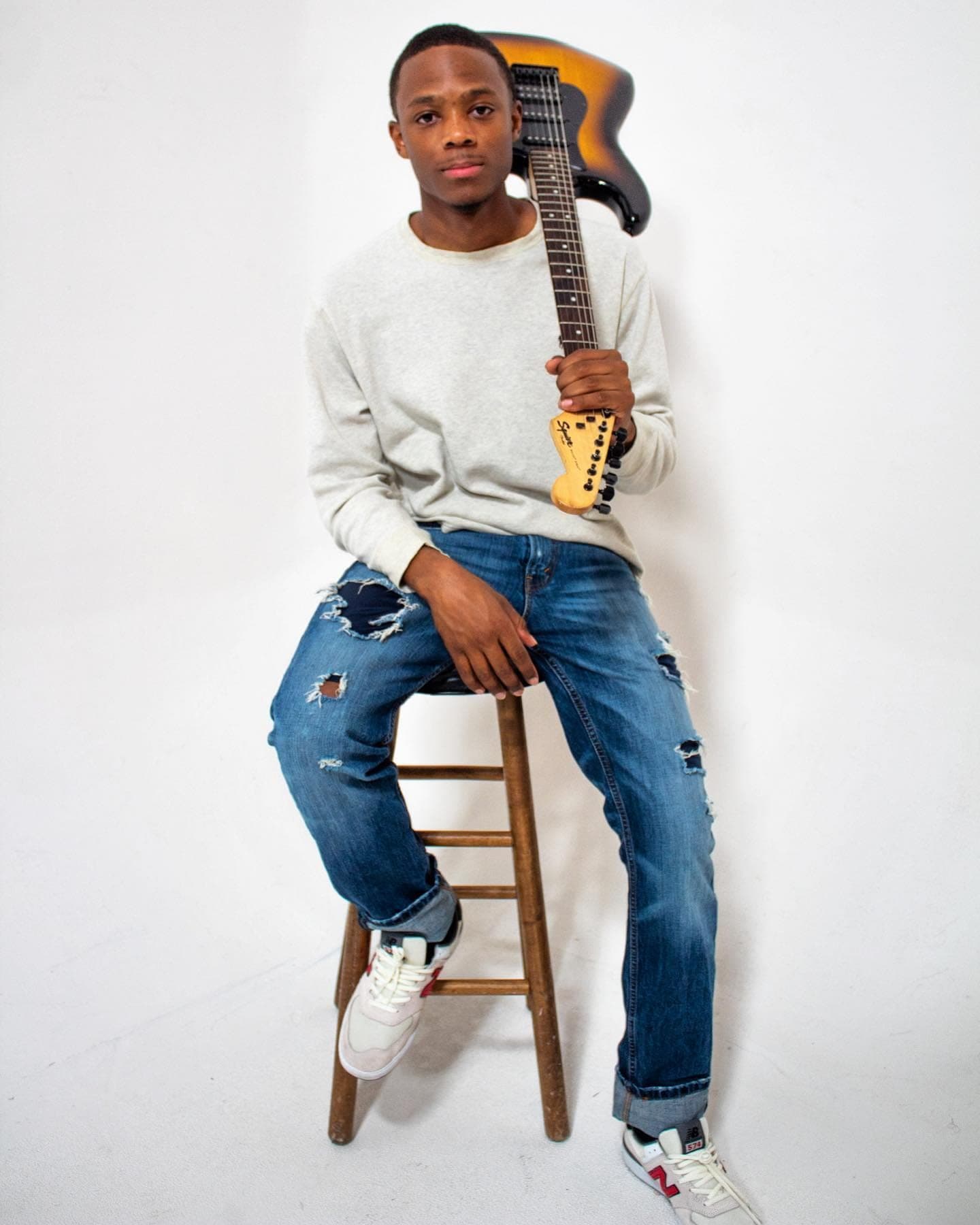 Paul Neil sitting on a wooden stool with a guitar over his shoulder