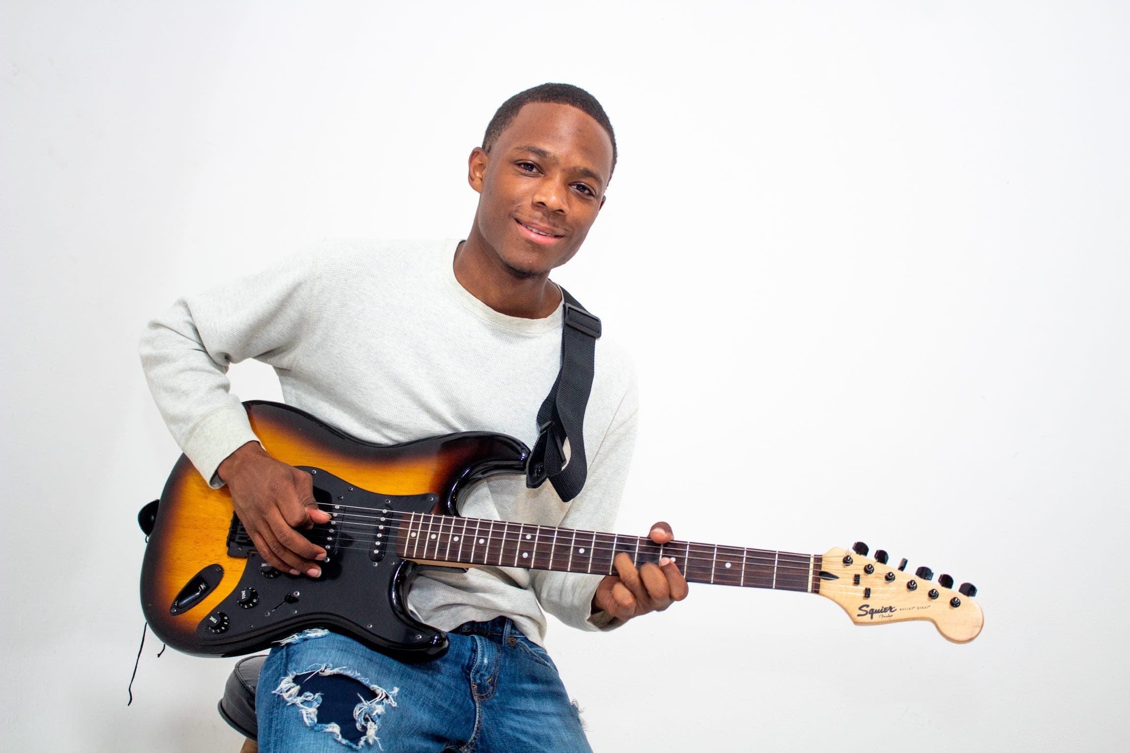 Paul Neil smiling with a sunburst guitar on a white background